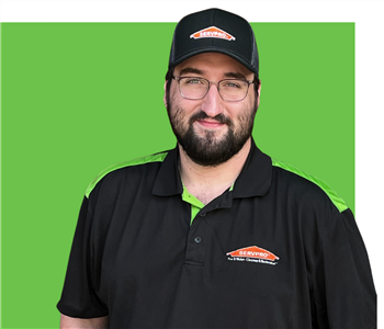 man in SERVPRO jacket and hat smiling with wooden background